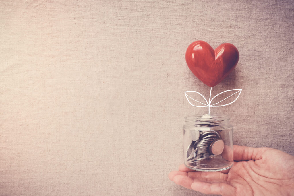 Hand holding a jar of heart tree growing on money coins, social